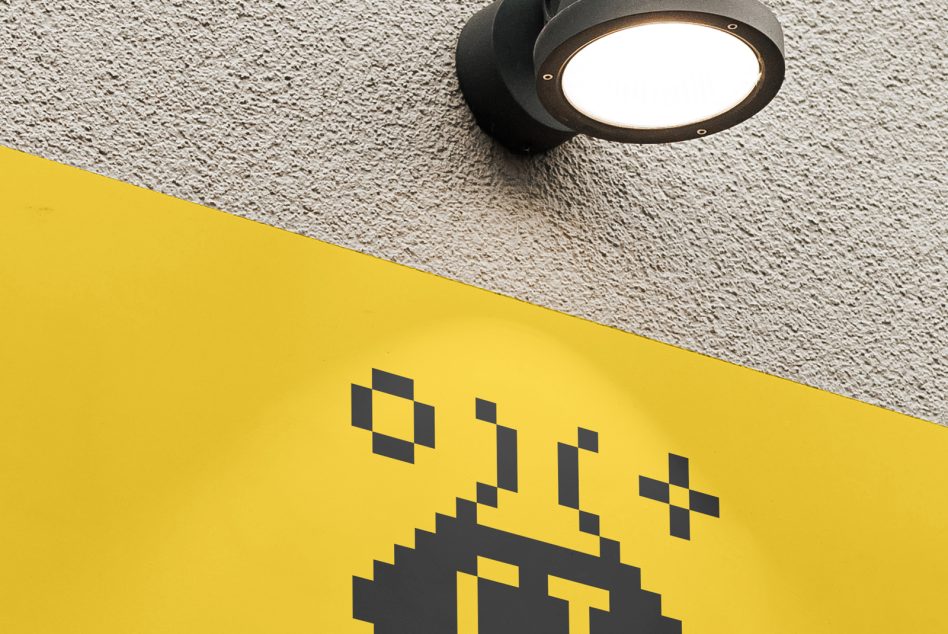 Wall-mounted spotlight illuminating pixel art graphic on yellow signage, displaying creative urban design, ideal for mockup or templates.